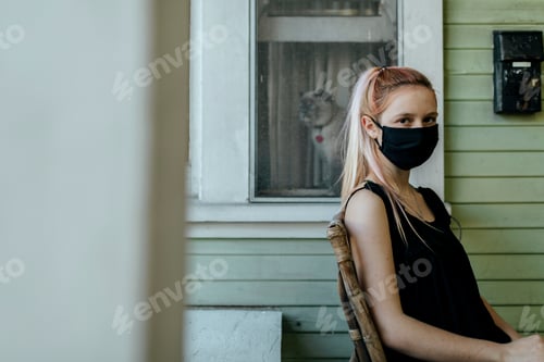 Preview: Girl wearing a mask sitting on her porch during the coronavirus lockdown.