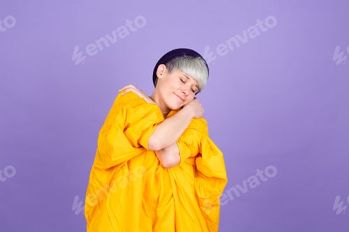 Preview: Stylish european woman on purple background self care hugging herself with smile and closed eyes