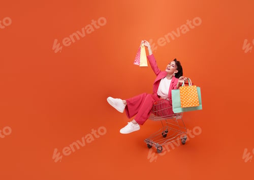 Preview: happy Fashionable woman sitting on trolley and shopping bags with shopping promotion summer sale