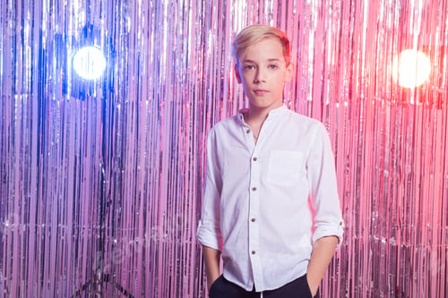 Preview: Awkward age and teenage concept - Portrait of teen boy at a party. Shiny background