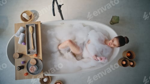 Preview: Serene woman relaxing foam filled bathtub top view. Tranquil lady enjoying spa