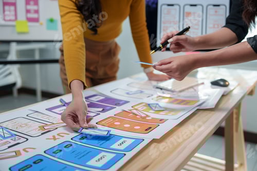 Preview: Two female ux designers are collaborating on a project, arranging wireframes on a table and discussi