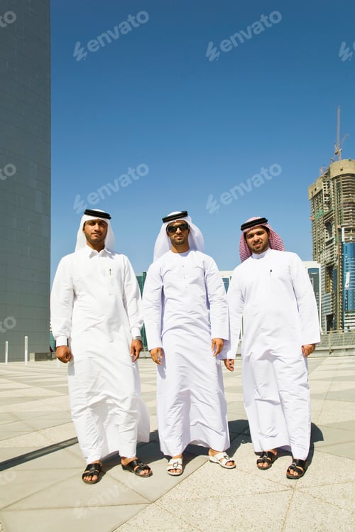 Preview: Three men dressed in traditional white thobes standing confidently under a bright blue sky.