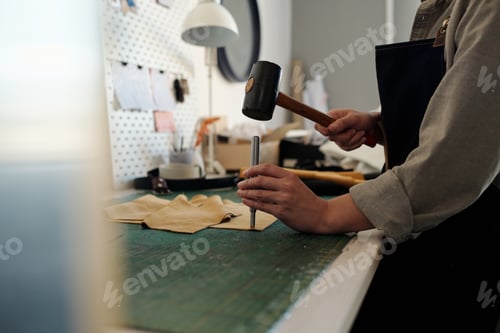 Preview: Professional young female tanner keeping hammer over small steel shaft