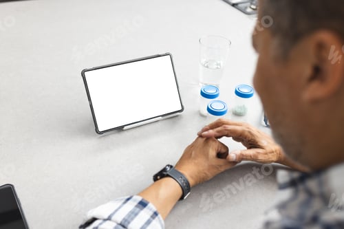 Preview: A senior man is seated at a table with medication and a digital tablet, with copy space