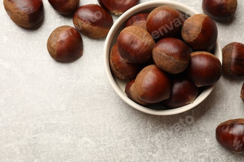 Preview: Bowl with roasted edible sweet chestnuts on light grey table, flat lay. Space for text