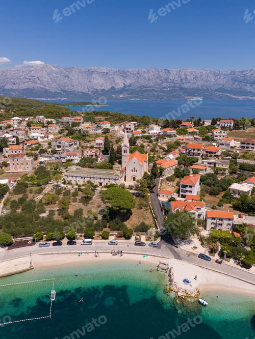 Preview: Aerial view of a coastal village with a church in Bol, Croatia, surrounded by mountains
