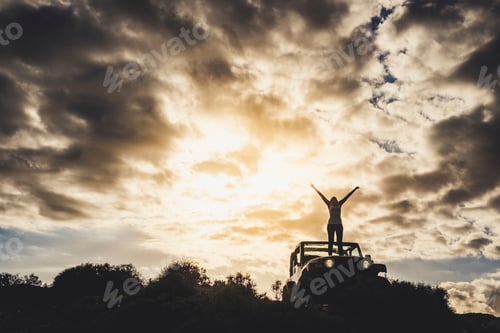 Preview: Success and lonely traveler concept with girl in silhouette standing on his car