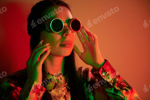 Preview: In retro pilot glasses. Fashionable young woman standing in the studio with neon light