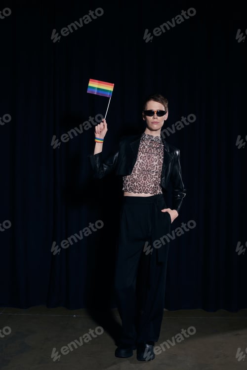 Preview: Full length of stylish nonbinary person in party outfit and sunglasses holding rainbow flag