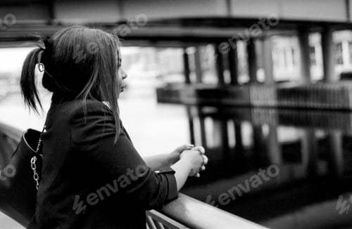 Preview: Businesswoman leaning on railing contemplating by water in monochrome analog style
