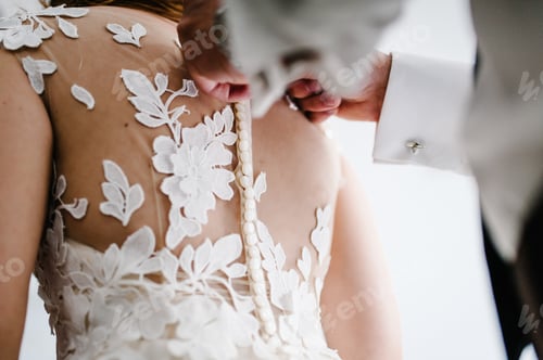 Preview: The man fastens buttons on the corset on the dress. Bride in white wedding dress with lace standing