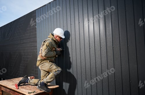 Preview: Builder installing corrugated iron sheet used as facade of future wooden frame house.