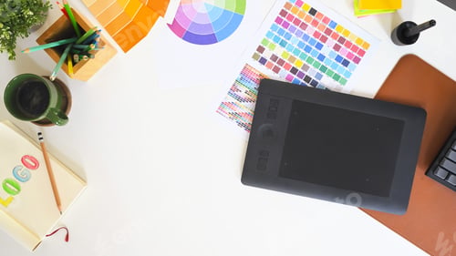 Preview: Top view of a graphic designer desk with color palette charts, drawing tablet, and coffee cup