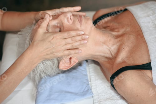 Preview: Senior woman enjoying rejuvenating face massage performed by professional beautician in spa salon
