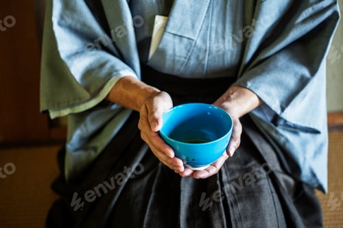 Preview: Man holding blue tea bowl during tea ceremony.
