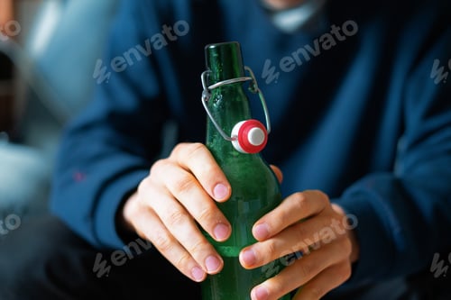 Preview: man holding the glass bottle of alcohol sitting at home in depression, bad habit problem