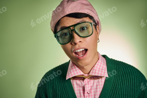 Preview: Stylish asian man showcases trendy fashion in vibrant green studio setting