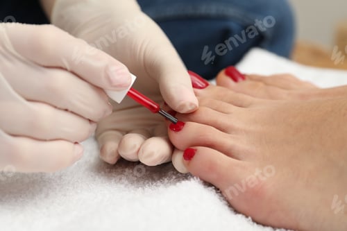 Preview: Pedicurist painting client`s toenails with red polish in beauty salon, closeup