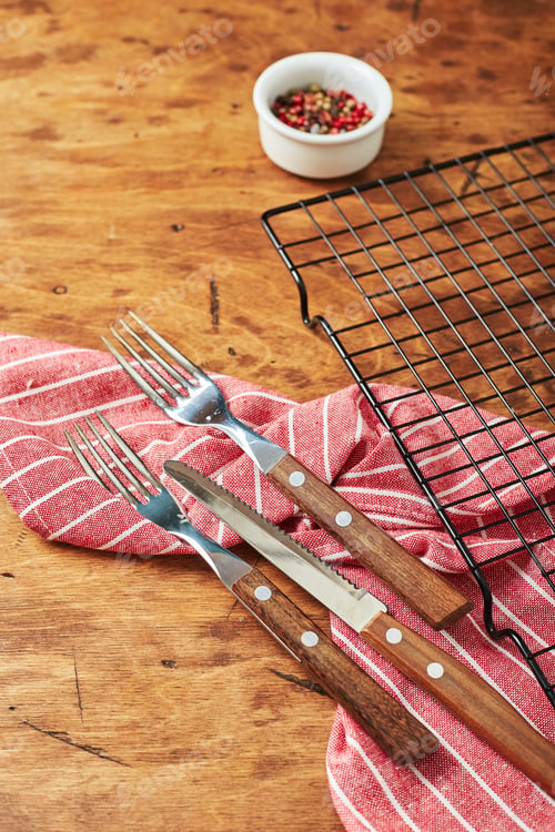 Preview: Forks, knife, napkin, empty baking rack and peppercorns in small bowl on wooden background