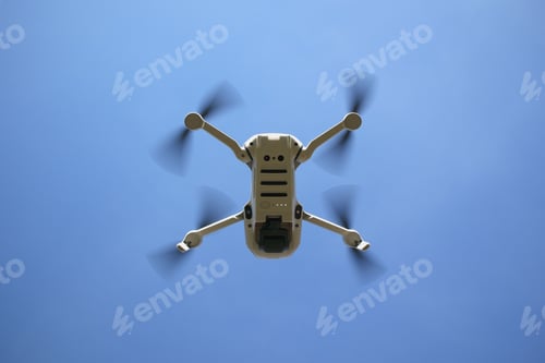 Preview: Low angle shot of a white drone with spinning propellers on a blue sky background
