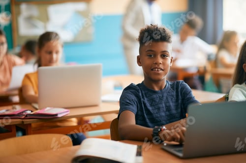 Preview: Smiling black elementary student using laptop while e-learning during class in the classroom