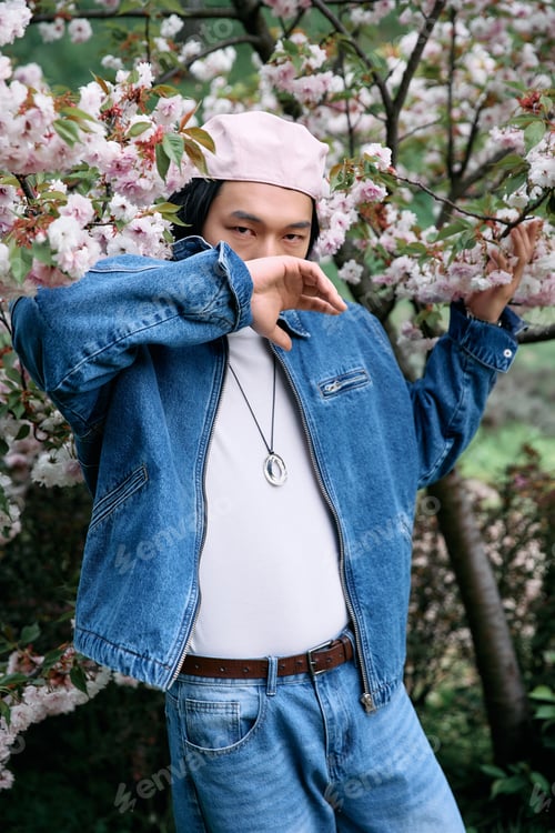 Preview: Stylish young man enjoying a serene moment in the park surrounded by blooming flowers