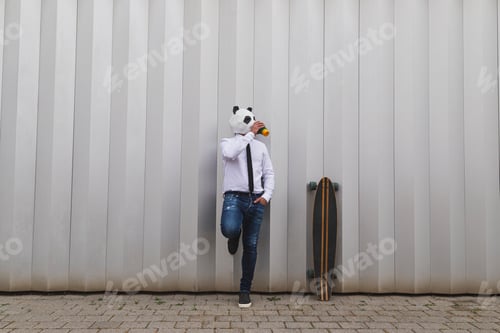 Preview: Businessman with a longboard skateboard and panda bear mask having coffee