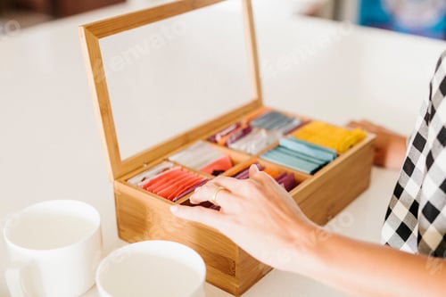 Preview: Close up of a woman standing in a kitchen, box of tea bags and mugs.