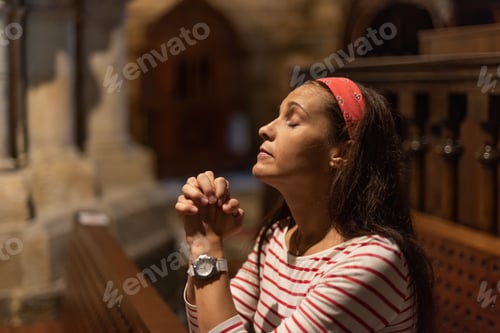 Vista previa: Hispanic woman praying with clasped hands in church