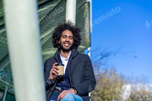 Preview: afro man with beard smiling positive standing at the street drinking a take away cup of coffee