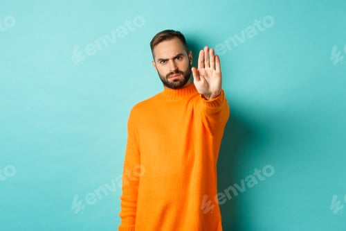 Preview: Serious frowning man showing stop gesture, telling no, prohibit and disagree, standing over light