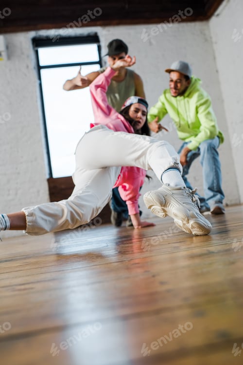 Preview: selective focus of girl breakdancing near emotional multicultural men