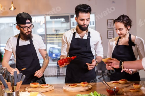 Preview: Cooking course - senior male chef in cook uniform teaches young people cooking class students to