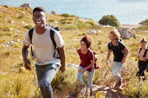 Preview: Millennial African American man leading a hike by the coast with friends, smiling to camera