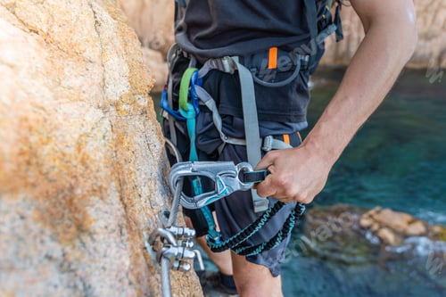 Preview: Climbing grips details young man's hand on rocks over the sea with rope and helmet.