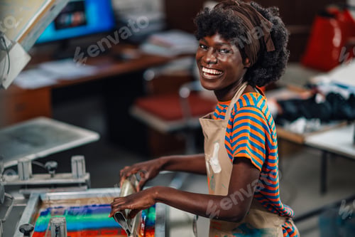 Preview: Smiling graphic technologist is screen printing with squeegee at workshop