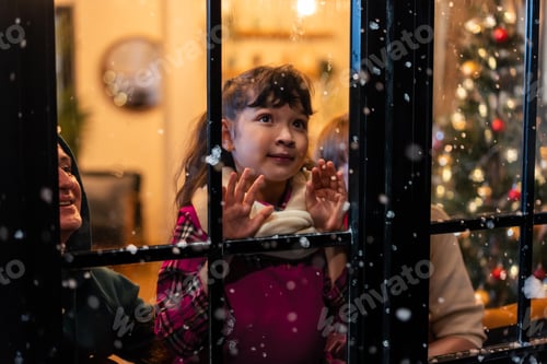 Preview: Adorable child looking at the window and first snow flakes with family. Y