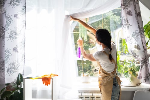 Preview: Woman in rubber gloves and apron manually washes window of house with rag cleaner