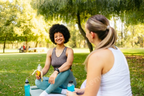 Preview: Two diverse women resting after outdoor training, smiling and refreshing