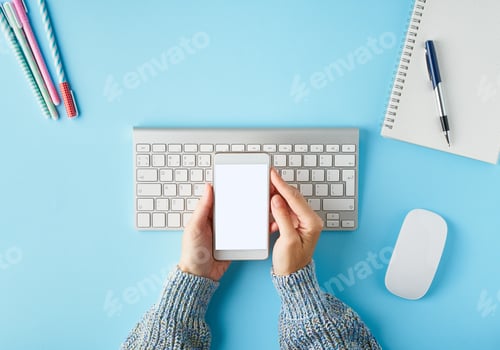 Preview: Mobile phone with blank white screen display in hand. Bright blue modern desk