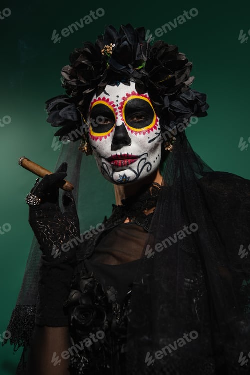 Preview: Woman in mexican day of death makeup and black costume holding cigar on green background