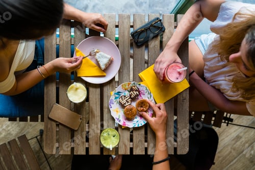 Preview: Top view of three young women sitting at wooden table with smoothies and biscuits