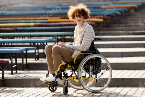 Preview: Nice guy in glasses is sitting in a wheelchair. The guy is holding a mobile phone in his hand.