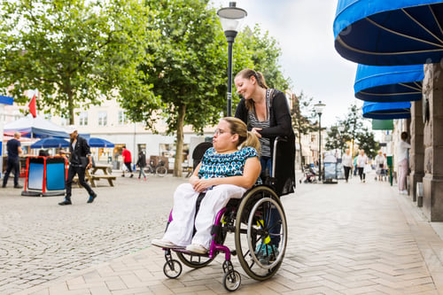 Preview: Assistant helping disabled woman in wheelchair move around city