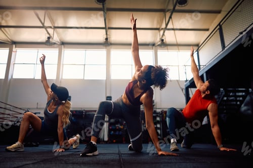 Preview: Group of athletes stretching while warming up during exercise class in a gym.