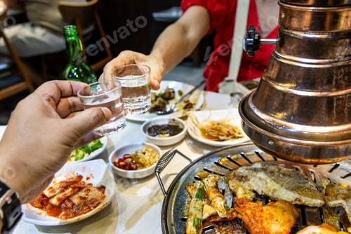 Preview: Two person toasting soju drinks during dinner in Korean barbecue restaurant while enjoying grilled