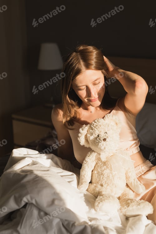 Preview: Girl is waking up in morning stretches in bed and sun shines from window. Happy young woman greets