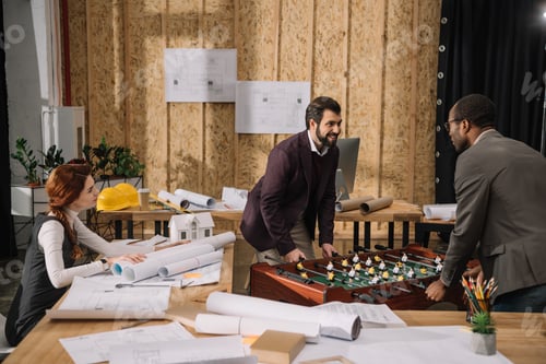 Preview: high angle view of young architects playing table football at modern office