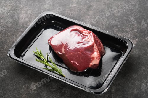 Preview: Beef steak. Fresh raw beef steak with fork and rosemary in vacuum black plastic pack on black stone